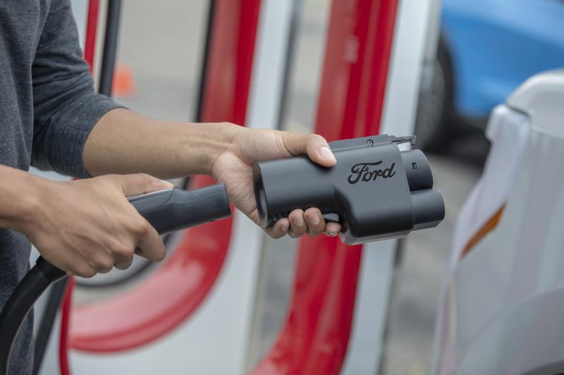 A person holding a Ford Fast Charging Adapter as they plug it into a charging cord.