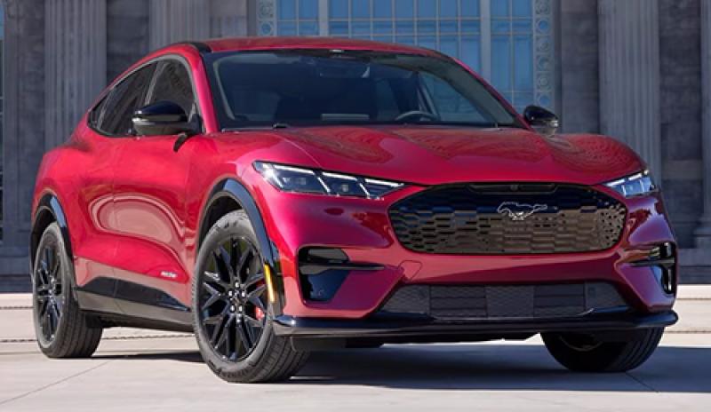 A red Mustang Mach-E® SUV is parked in the sunlight in front of a building.