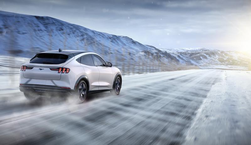 The Mustang Mach-E® kicks up snow while driving on a wintry road out in the foothills.