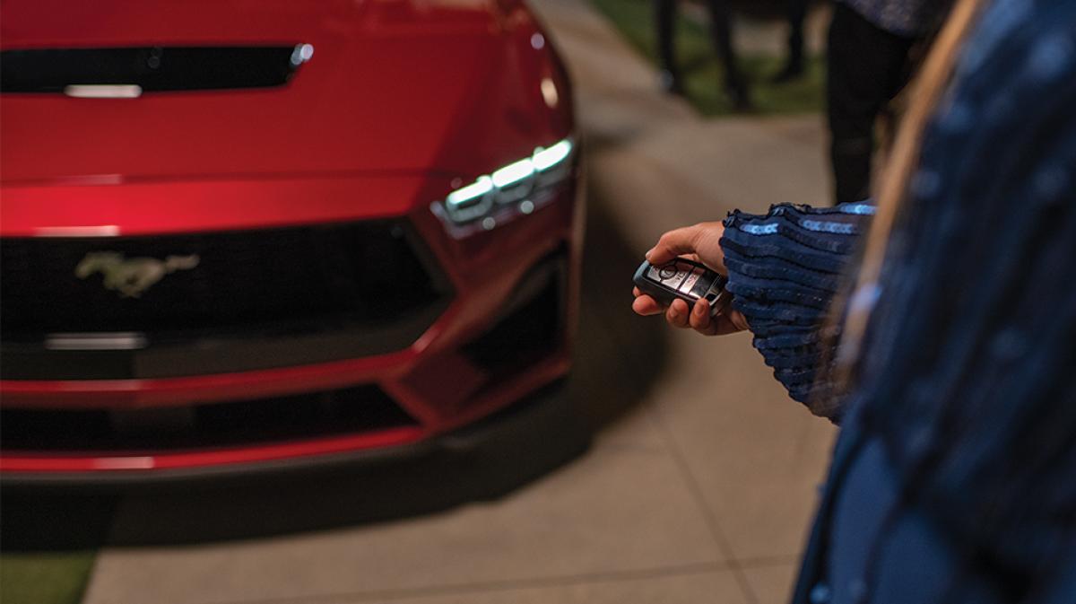 An owner stands in front of their Mustang® coupe, key fob in hand, with the coupe’s headlight illuminated